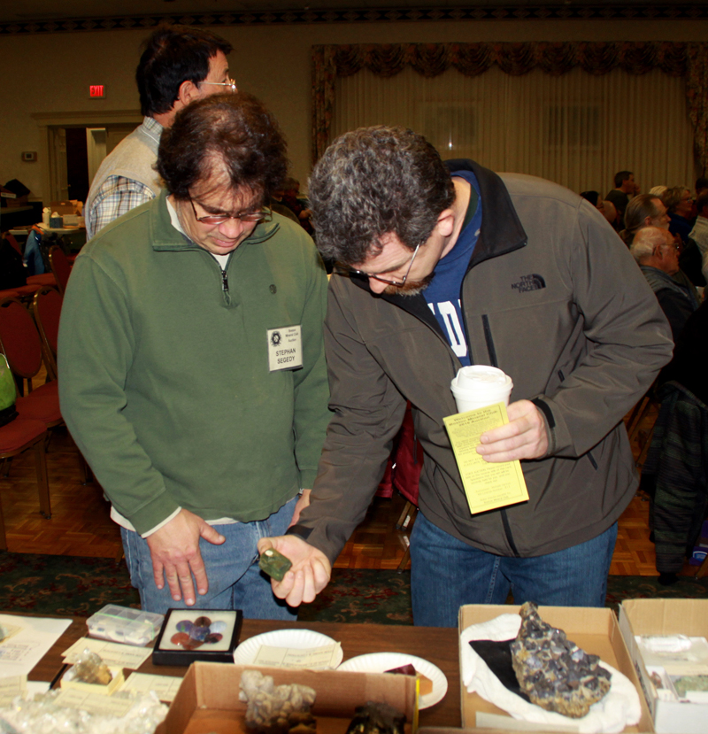 Two attendees examining a green mineral at a table full of mineral specimens